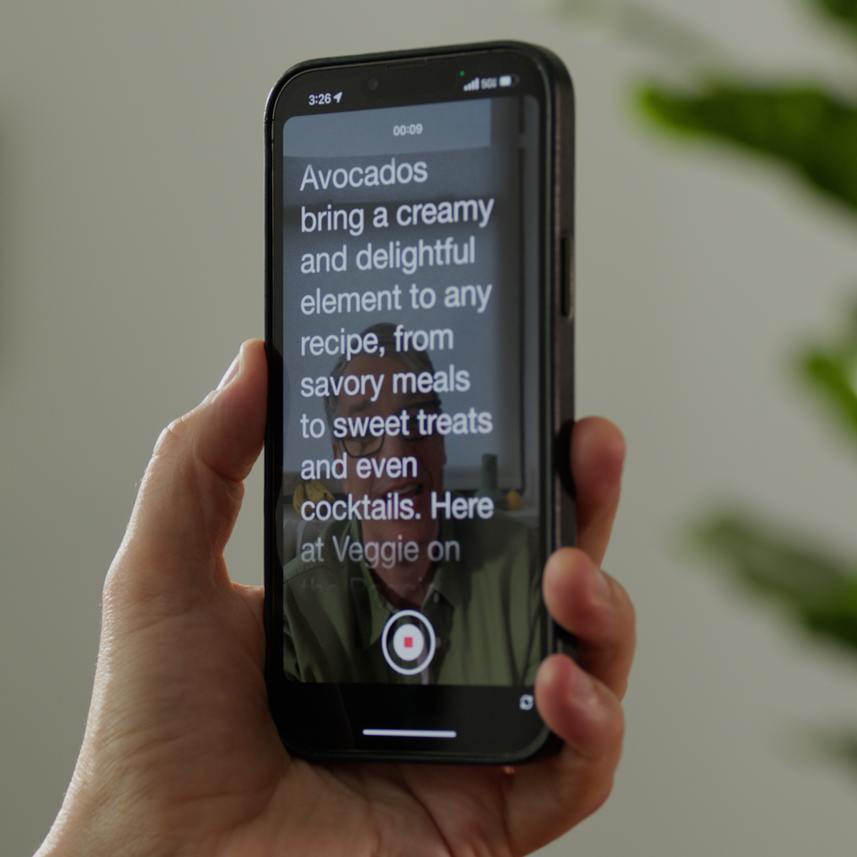 Person's hand holding a mobile phone with a screen showing a video teleprompter and record button