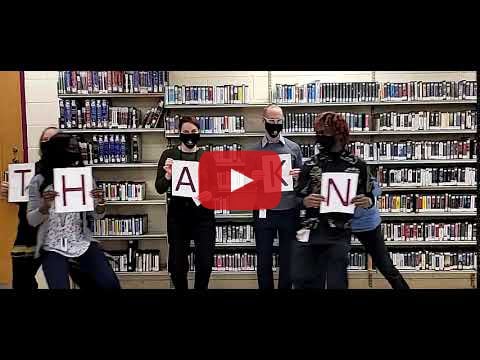 A bunch of library staff wearing masks and holding up letters that spell thanks.