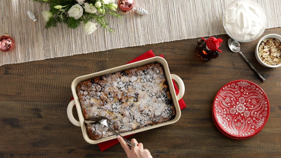 Overhead shot of a baked panettone bread pudding dusted with powdered sugar, holiday table setting