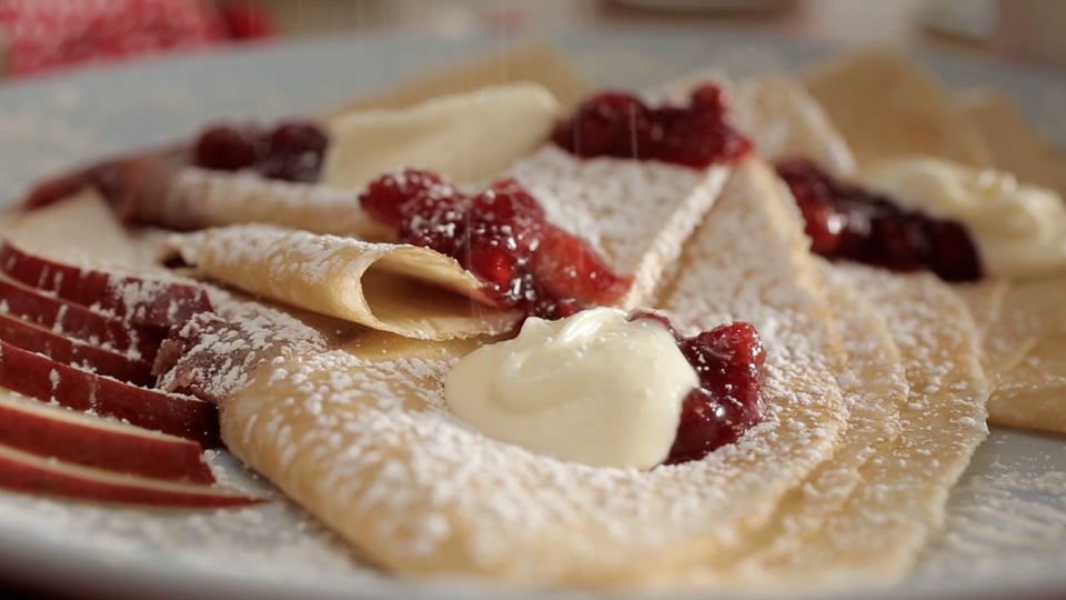 Close-up of crepes topped with berry compote and whipped cream