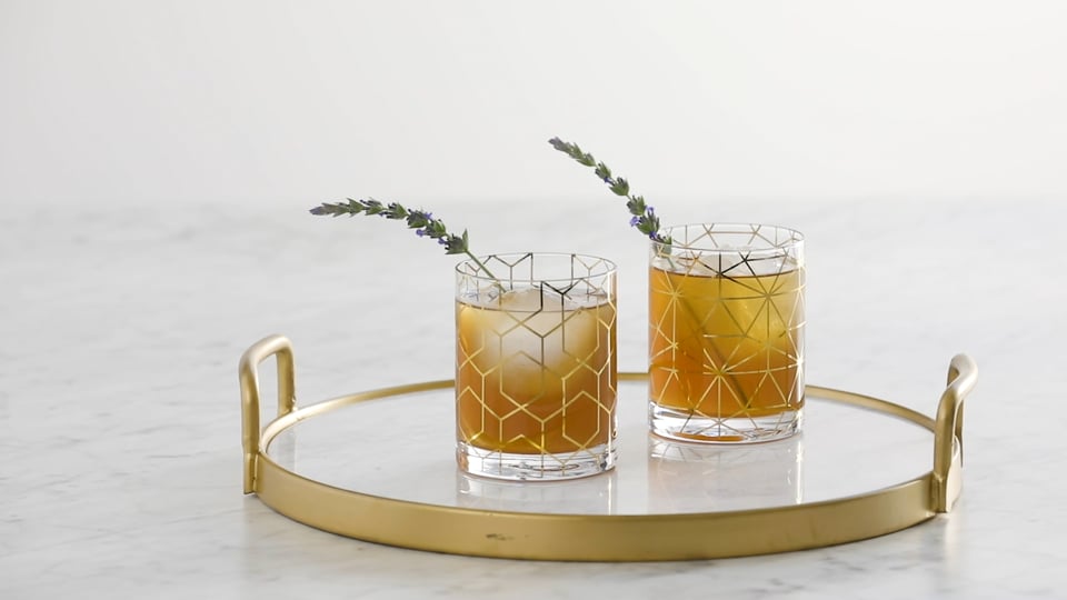 Two craft cocktails garnished with lavender on a marble and brass tray