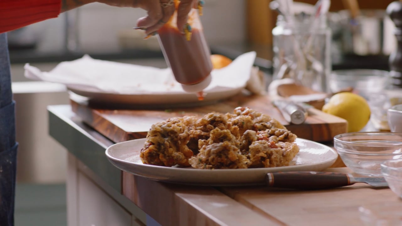 Sauce being poured over a plated dish in a kitchen, from Tastes Like Homecoming.