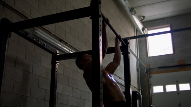 A fit young athlete exhaustively exercises from the pull up bar. 