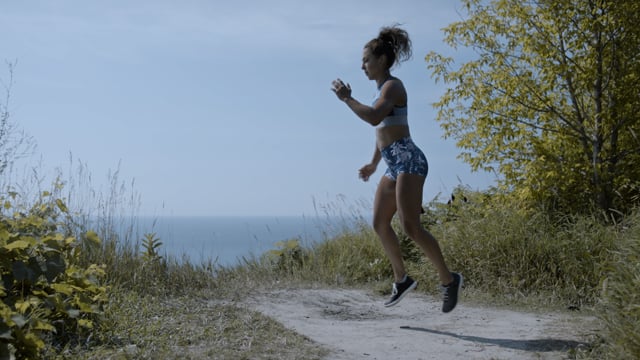 Working hard. A powerful and confident woman does lunges on a cliff's edge. Focused and determined.
