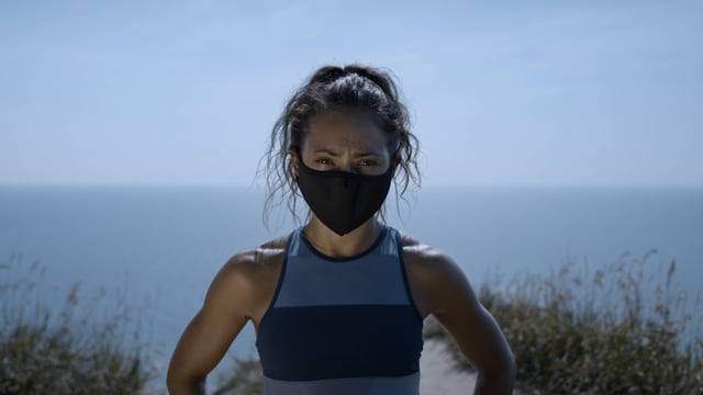 Top of the world. Portrait of an athletic woman on a cliff's edge in a mask. Working out with a mask on. Pandemic exercising.