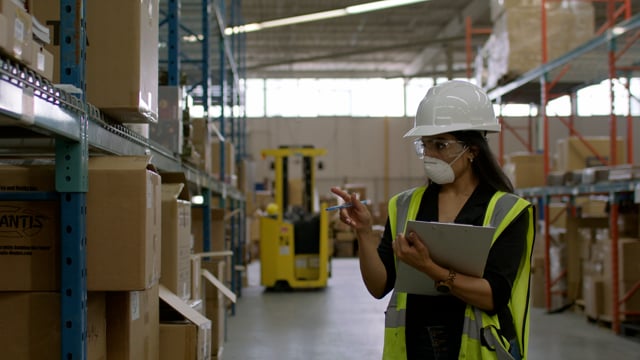 An industrial warehouse manager reviews inventory as it goes out for delivery.
