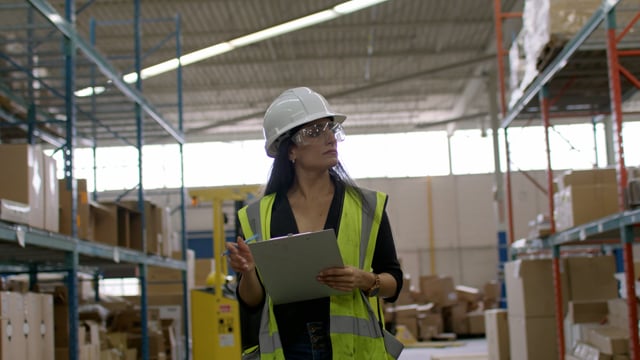 A female industrial warehouse manager reviews inventory as it goes out for delivery.