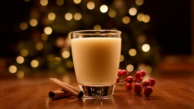 An inviting glass of seasonal eggnog sits in front of the christmas tree. 