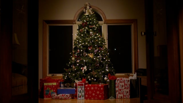 A beautifully decorated christmas tree is adorned with decorations and sits with gifts around it ready for the holidays .