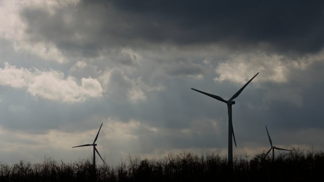Green energy windmills silhouetted against a cloudy sky. 