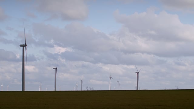 Beautiful clouds float in the sky above a fleet of green energy windmills standing in a rural field.