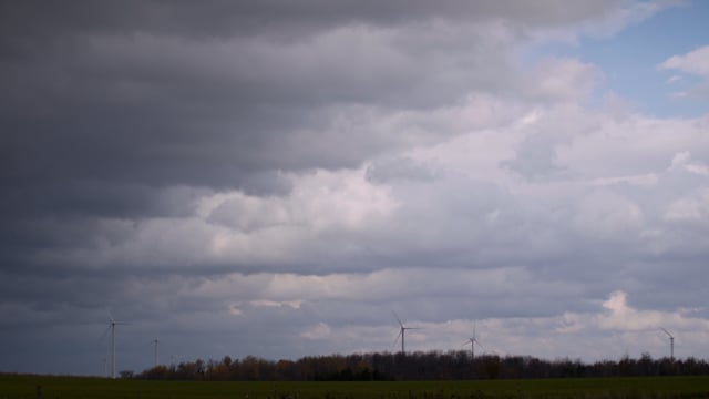 The dark skies of a storm over a rural field peppered with windmills generating green energy.  