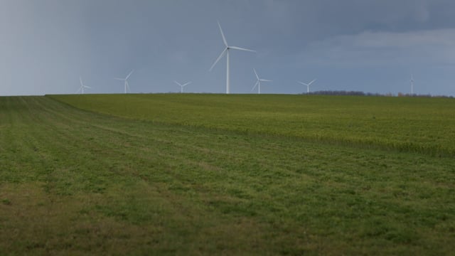 Beautiful skies above a fleet of green energy windmills standing in a rural field.