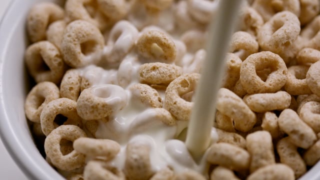 Pouring rich and nutritious farm fresh milk over a big bowl of healthy whole grain cereal. 