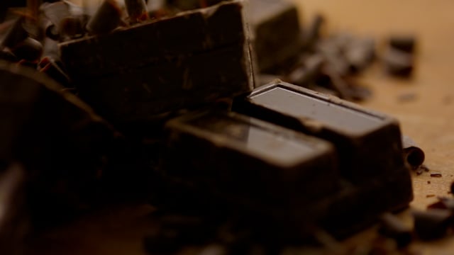 Decadent blocks of artisanal chocolate are sprinkled with chocolate shavings in slow motion.