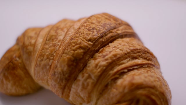 Fresh baked flakey croissant being brushed with rich melted butter.  