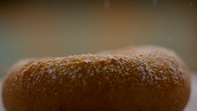 A freshly made doughnut being dusted with sweet decadent icing sugar. 