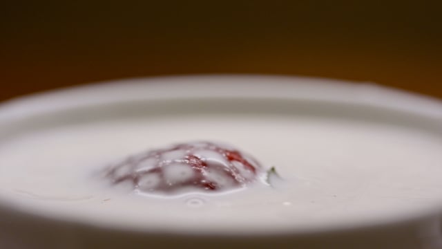 Macro shot of juicy organic strawberries splash into a dish of rich, decadent cream.