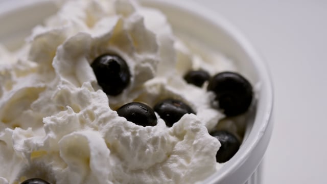 Sweet and fluffy whipped cream fills a bowl as we prepare a decadent dessert, topped with rich and juicy farm-fresh berries. 