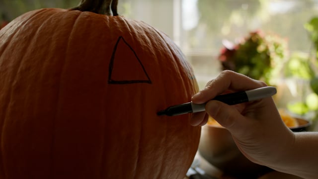 Prepping a jack-o-lantern for carving by drawing a face on a pumpkin. 
