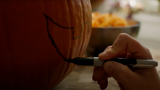 Drawing out the mouth of a jack-o-lantern on a pumpkin for Halloween. 