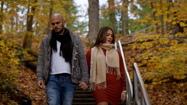 A young couple hikes down a set of stairs deep in the woods, surrounded by autumn colours. 