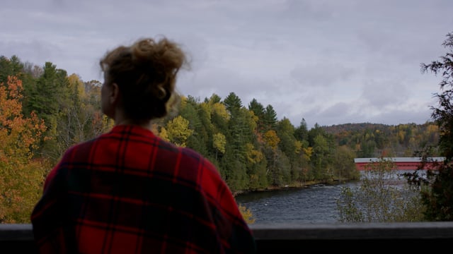 A beautiful young woman sips coffee while taking in the majestic view of an autumnal river scene. 