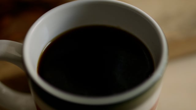 Cream pouring into black coffee. Slow-motion cream pouring into a mug of black coffee.