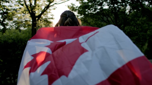 A woman runs for joy with a Canadian flag behind her for independence day. Slow-motion flowing in the breeze.