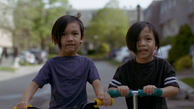 Two young brothers learn to ride a bike and scooter together. Family life. Childhood.