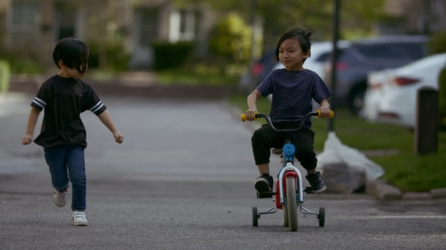 Brothers playing in the street. Learning to ride bike. 