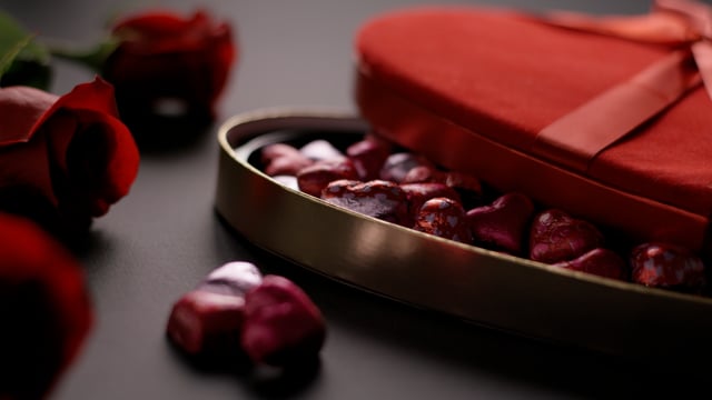 Heart-shaped box of chocolates on a wooden tabletop with roses. Static with light fading in and out. 