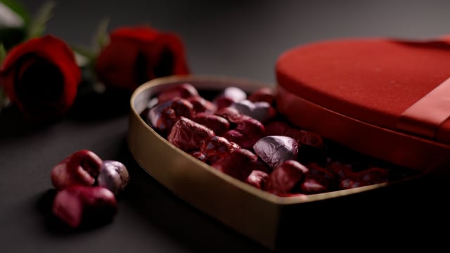 Heart shaped box of chocolate on wooden table with roses. Close-up with subtle camera movement. 