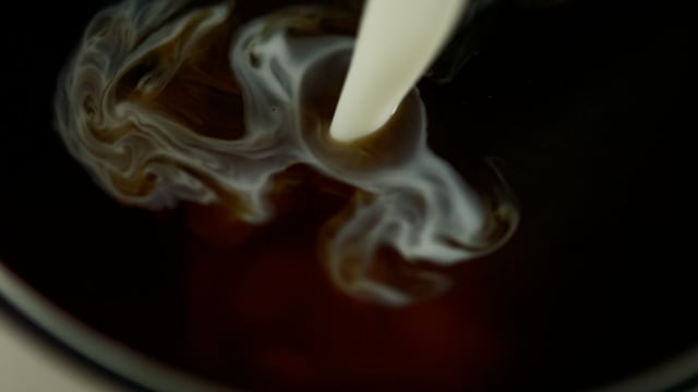 Cream pouring into black morning coffee. 