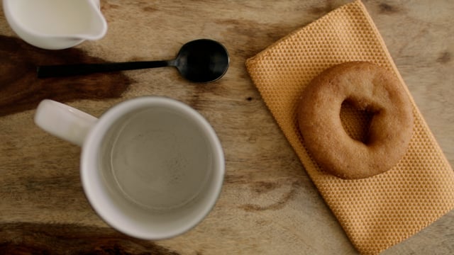 Doughnut and black coffee pouring into mug. Layflat of black coffee pouring into a mug with a doughnut beside it.
