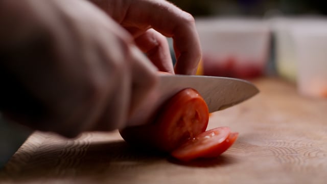 A talented chef slices tomatoes as they prepare for a delicious meal. 