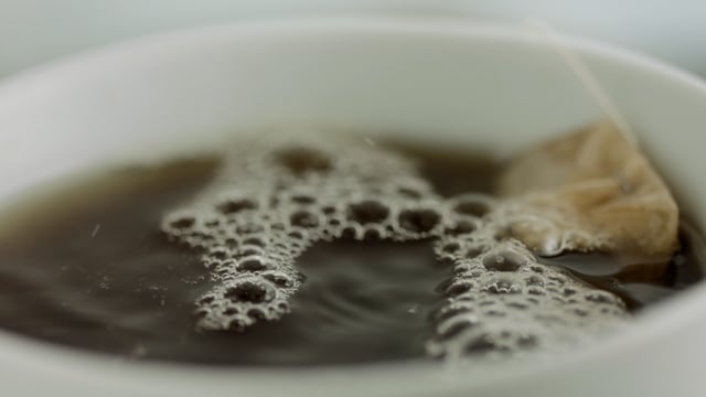 Teacup closeup. Adding water to a white cup of tea. Morning scene. 