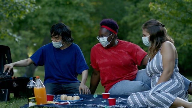 A group of friends celebrate national holiday in a park with a bbq while wearing masks.