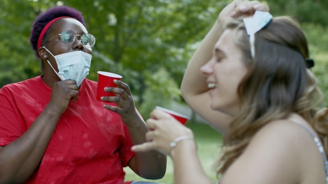 Trying to cheers with masks on due to global pandemic. A diverse group of friends in a park celebrating.