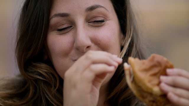 A young woman enjoying a delicious hamburger from a local independent  restaurant. 