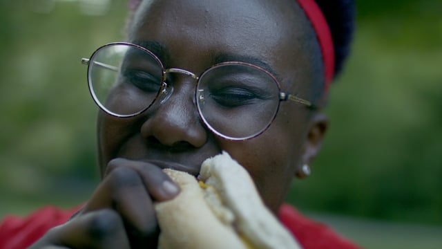 A black woman takes a big bite of a hotdog. Full of joy having a bbq with friends.