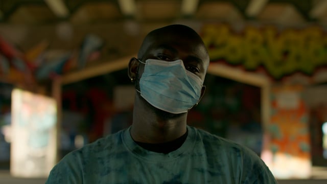 A portrait of a black man wearing a medical mask at an urban underpass. 