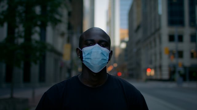 A black man downtown wearing a medical mask for pandemic protection. 

