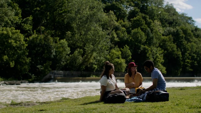 Millennials meet in a beautiful park to hang out and read. Chilling beside a river in a diverse group.  