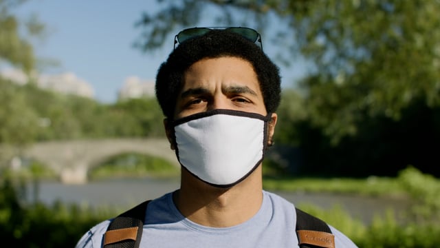 A portrait of a handsome man wearing a mask and looking confident in a park.