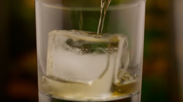 Whiskey pouring over ice in a tumbler.