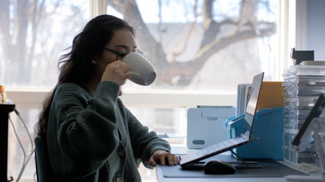 A young entrepreneur runs her business from her at home office while enjoying a cup of coffee. 