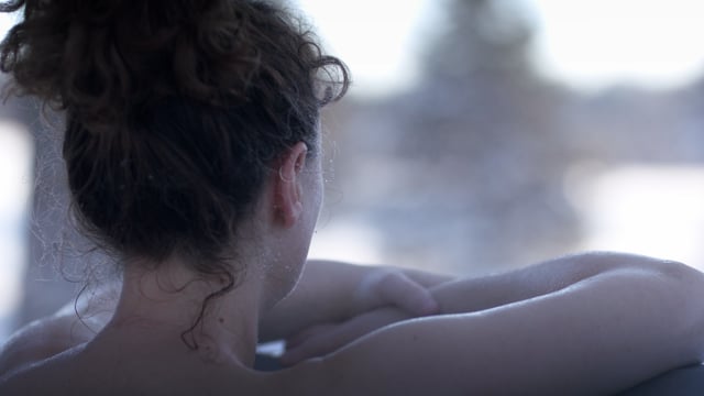 Woman looking out at nature while in a hot spring at a nordic spa. 