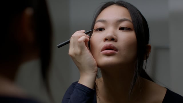 Young woman putting on her eyeliner in the mirror.