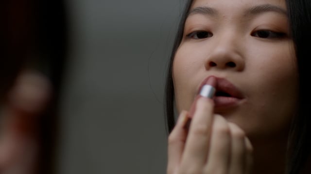 Young woman putting on her lipstick in the mirror.